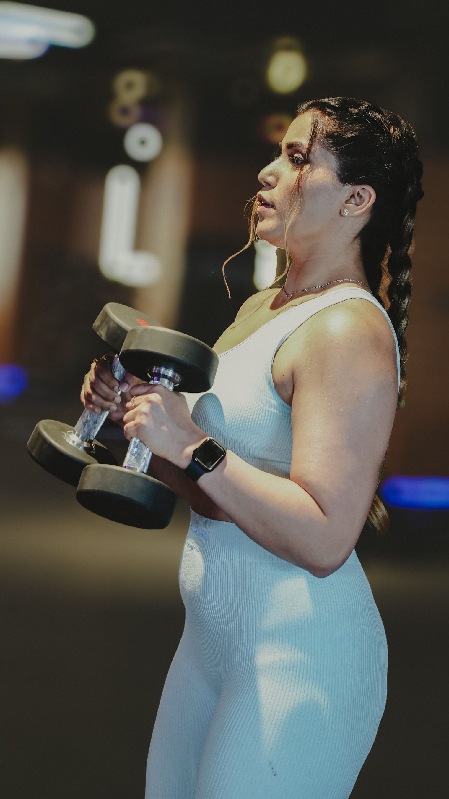 A woman holds a pair of generic dumbbells in a gym; neither adjustable dumbbell model in the comparison is pictured.