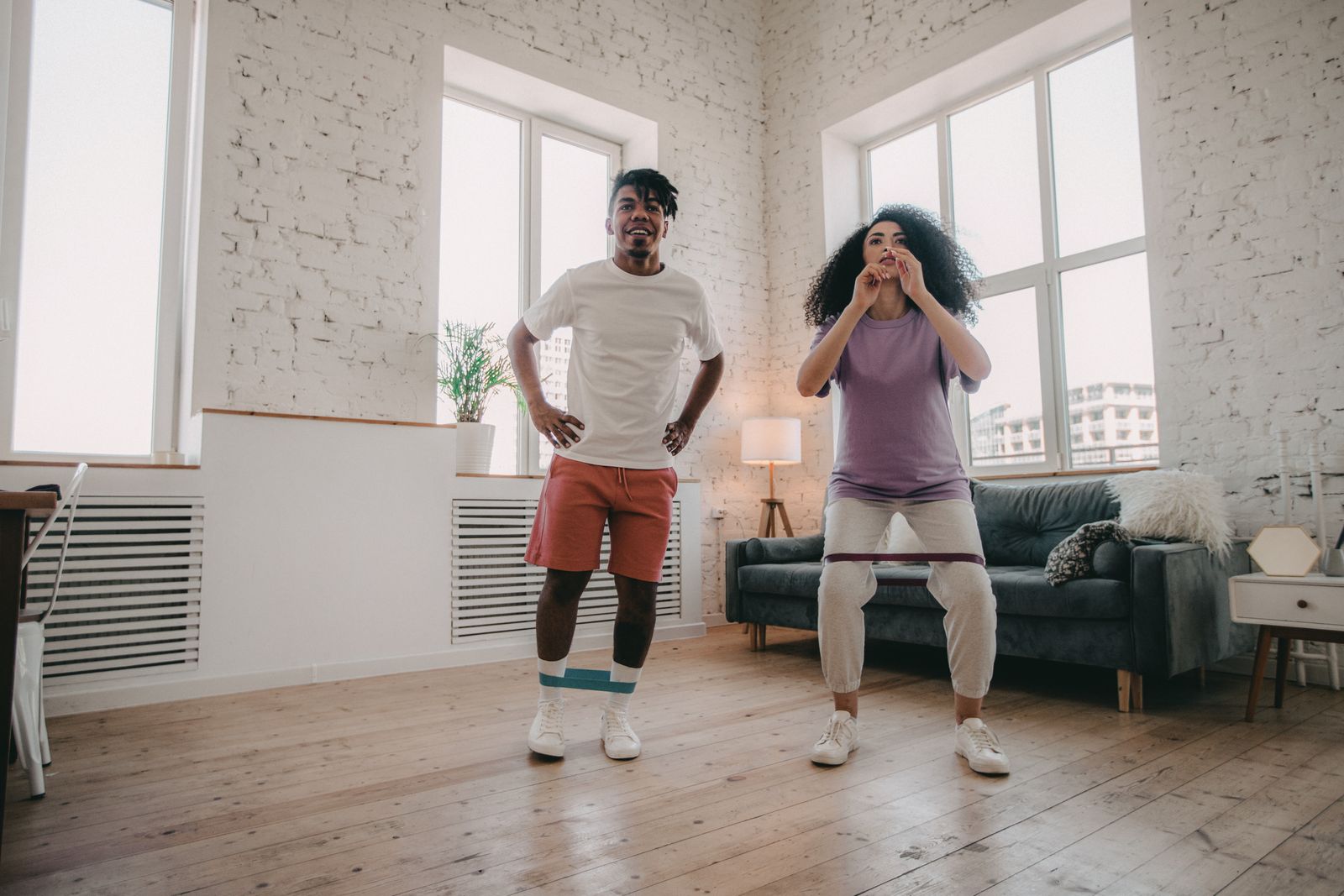 Two adults exercise at home using resistance bands; the scene is illustrative, not a training demonstration.