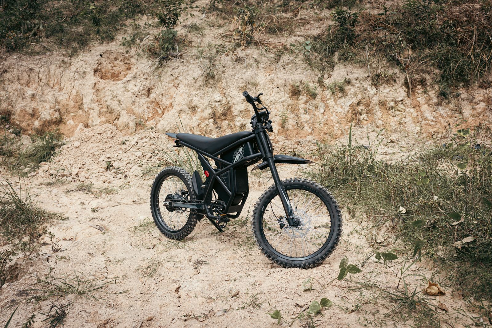 A black electric dirt-style bike stands on rocky terrain; the image does not establish its legal classification or suitability for a route.
