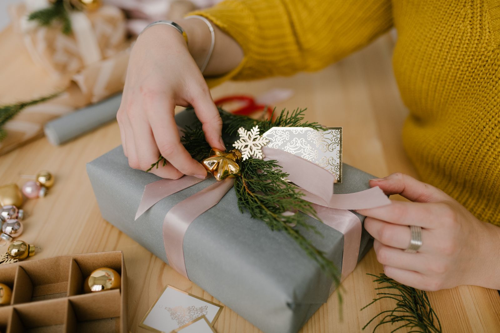 Hands carefully wrap a holiday present with ribbon and festive paper.