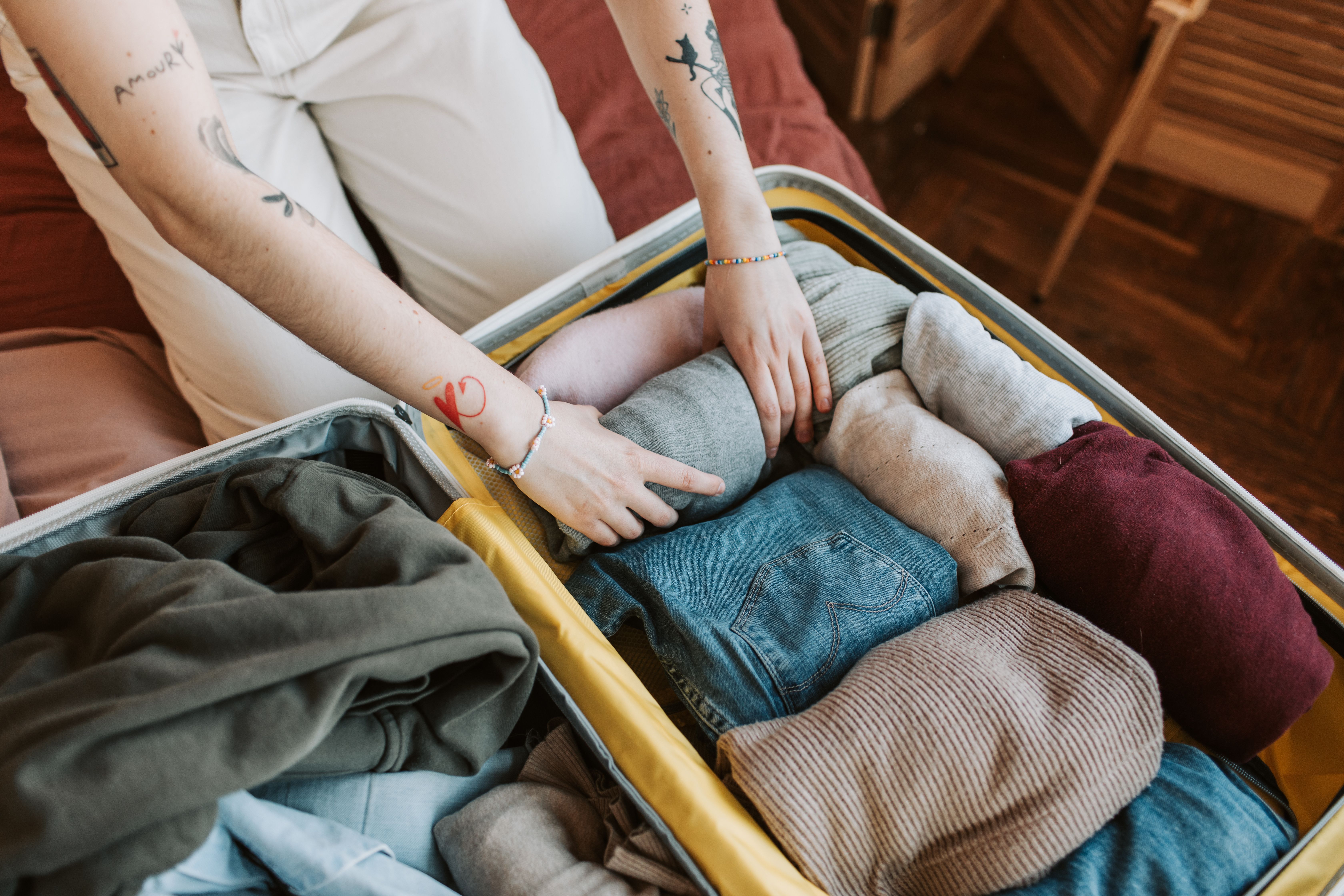 Hands pack folded clothes into an open suitcase on a bed.