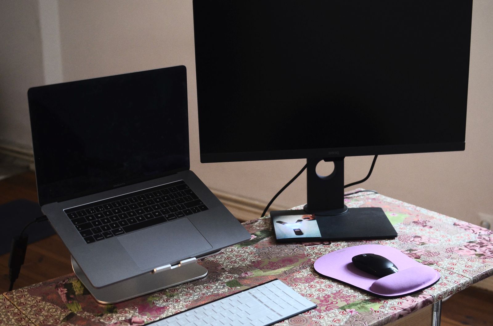 A laptop sits on a stand beside keyboard and mouse on a desk; the setup is illustrative.