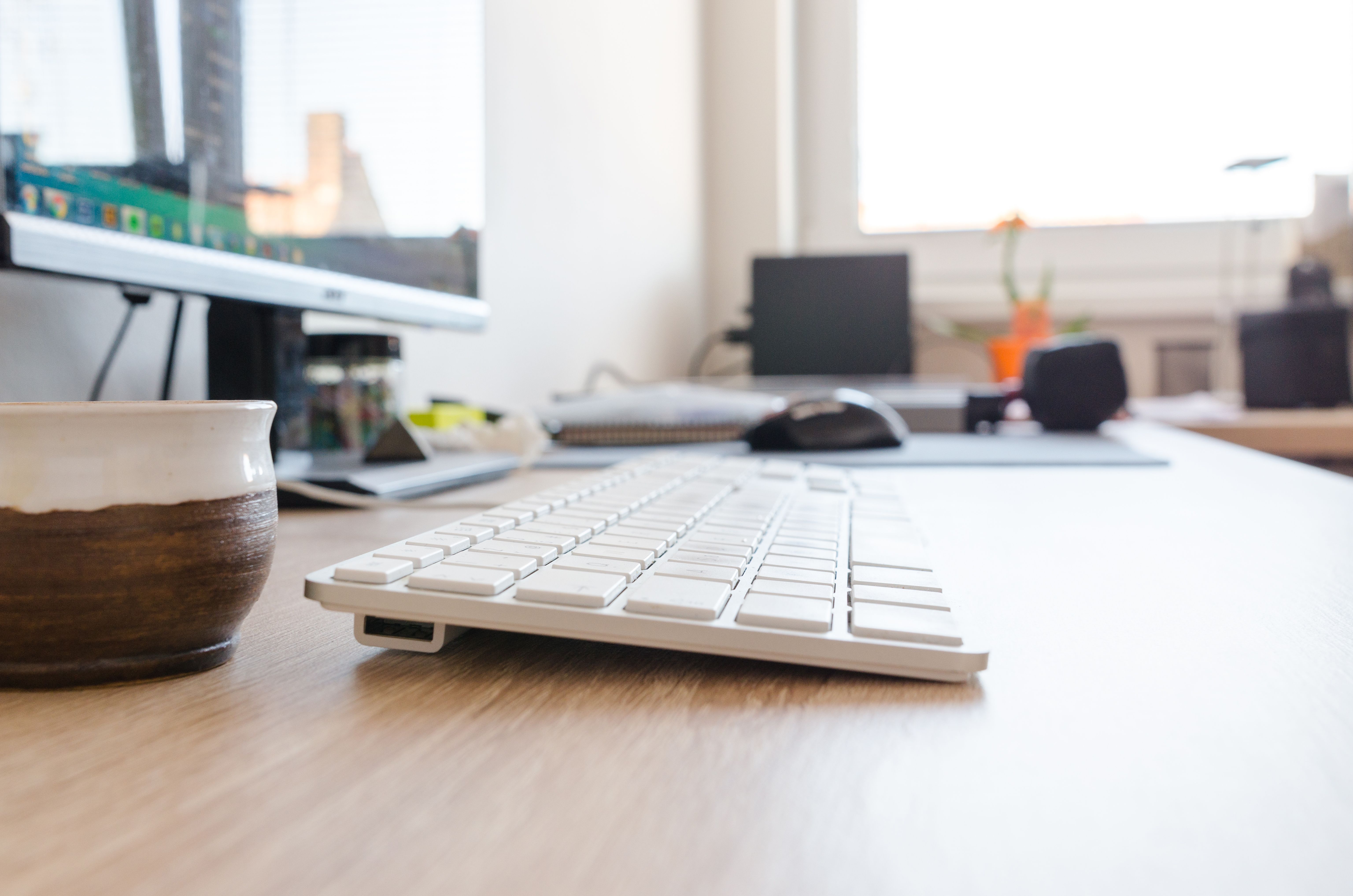 A real office desk with a white keyboard and monitor; the keyboard is illustrative and is not identified as either model compared here.