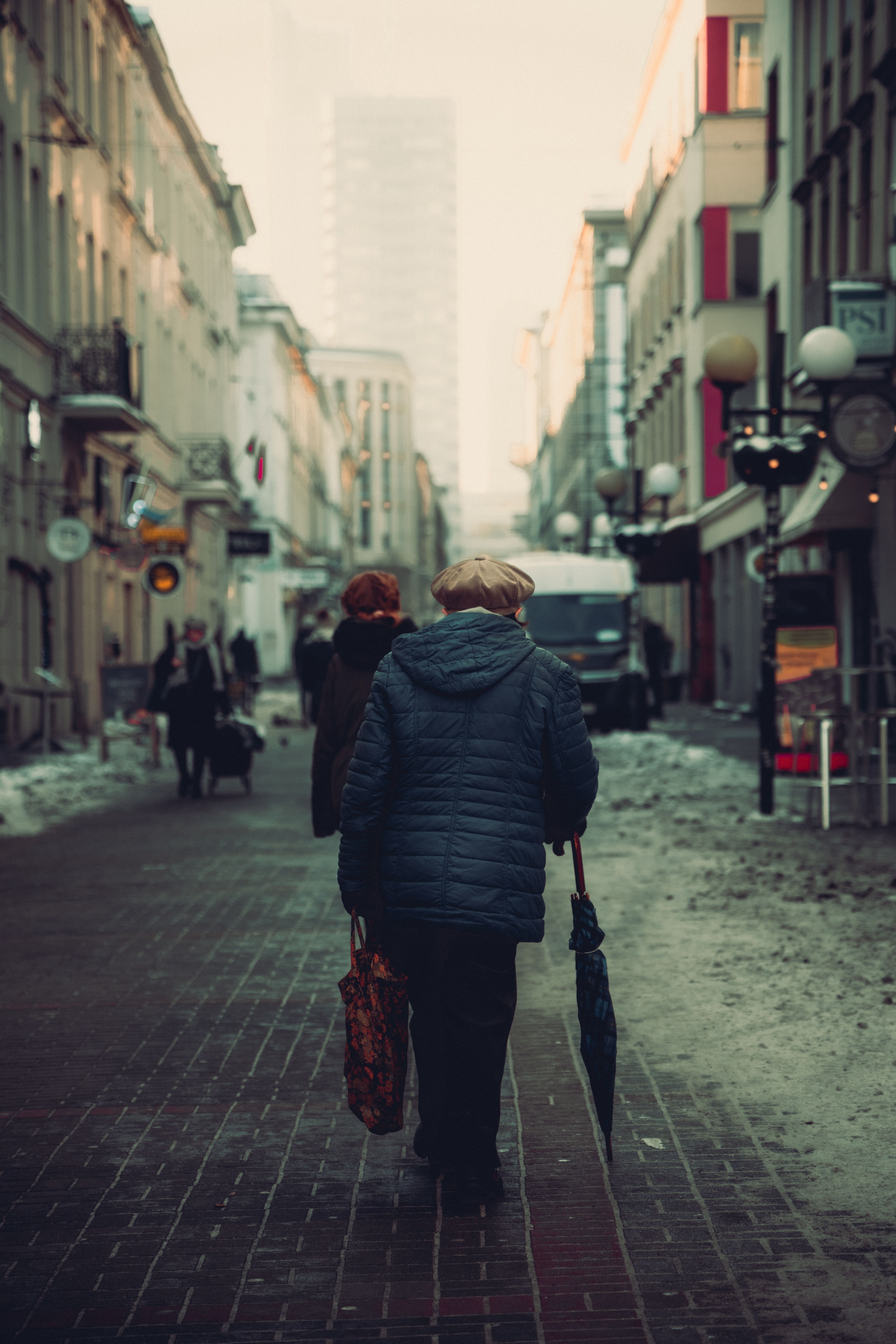 A person in a dark puffer jacket walks along a snowy city street; the coat is not identified as either compared product.