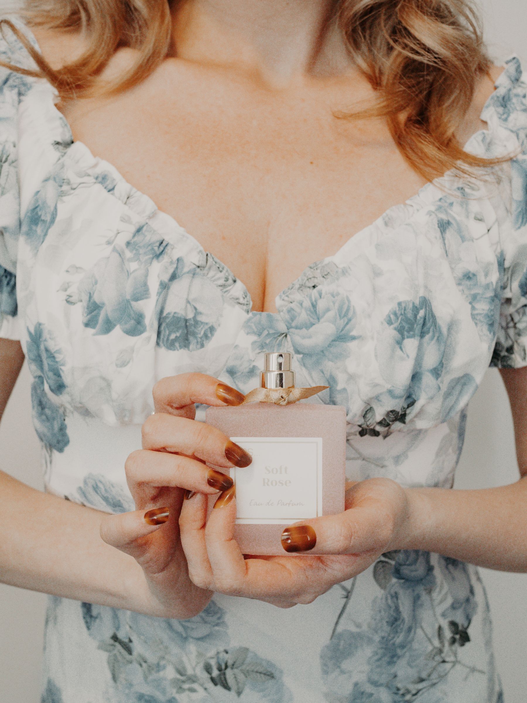 A person holds a perfume bottle in a softly lit room; the bottle is not either fragrance in this comparison.