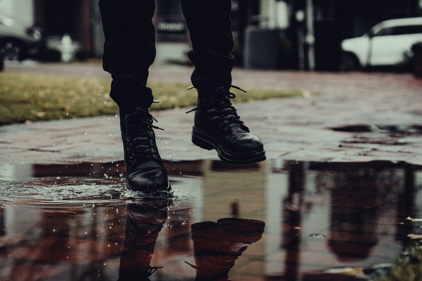 Close-up of black lace-up boots splashing through a rain puddle; the photo illustrates footwear but does not verify waterproofing or traction.